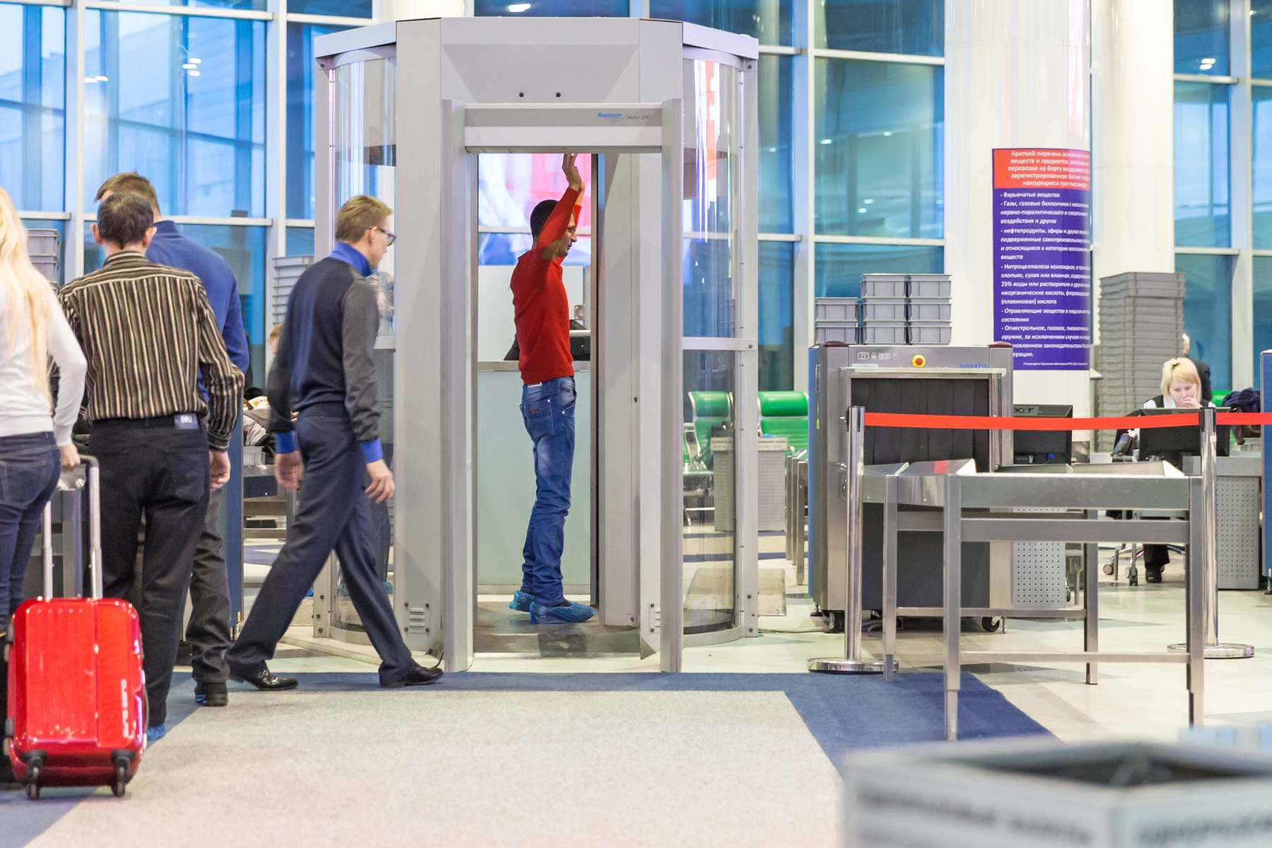a male passenger standing in a full-body scanner at airport security, having booked a window seat on a plane