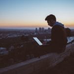 Man sits on wall using free internet abroad while on laptop