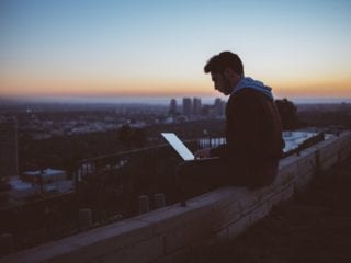 Man sits on wall using free internet abroad while on laptop