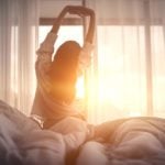 Woman who prioritizes sleep hygiene wakes up to the sun through a curtained window.