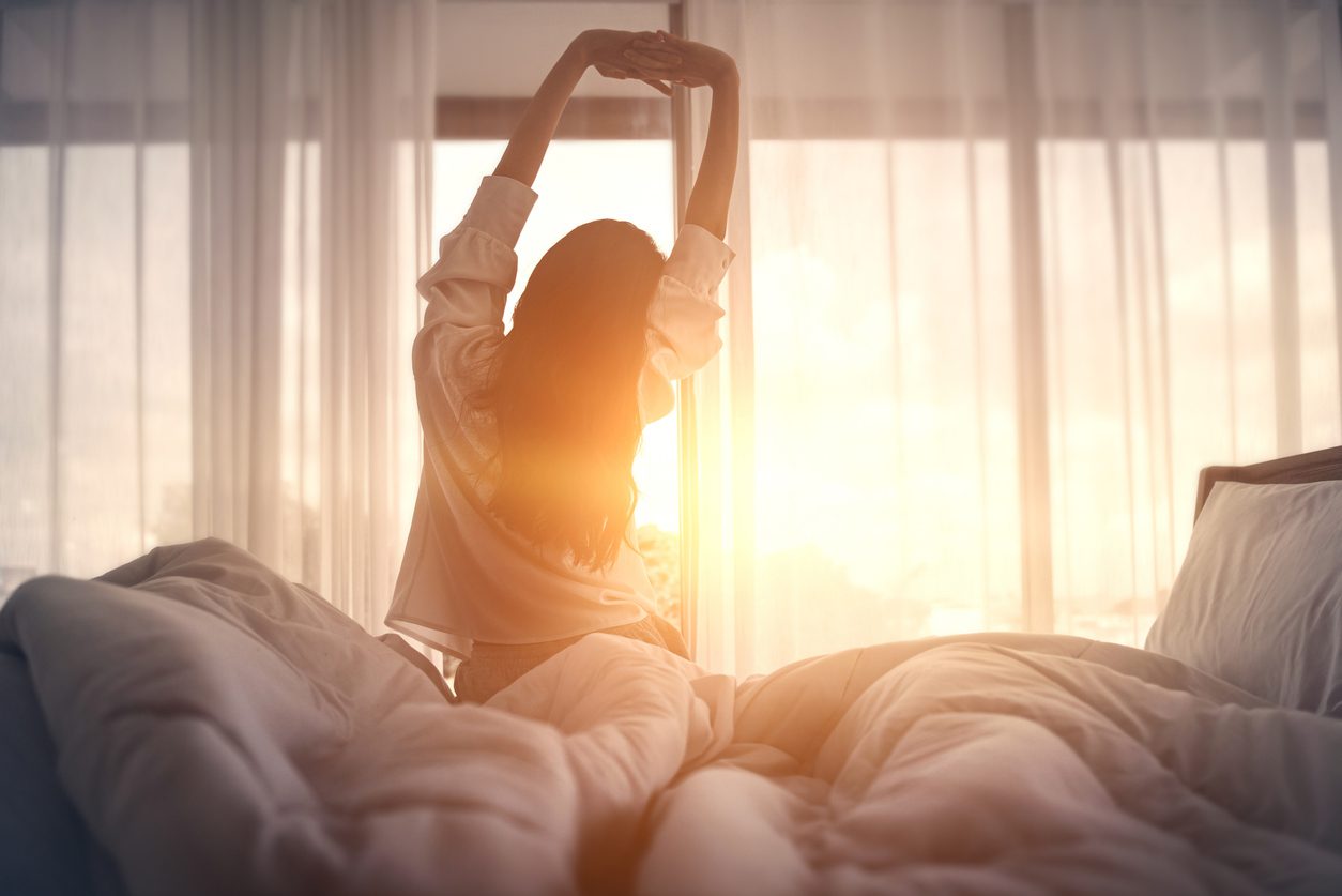 Woman who prioritizes sleep hygiene wakes up to the sun through a curtained window.