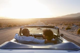Rear view of an expat and spouse of expat driving into the sunset in a classic convertable
