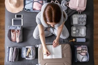 Expat sitting on a bed planning out her packing list for moving abroad.