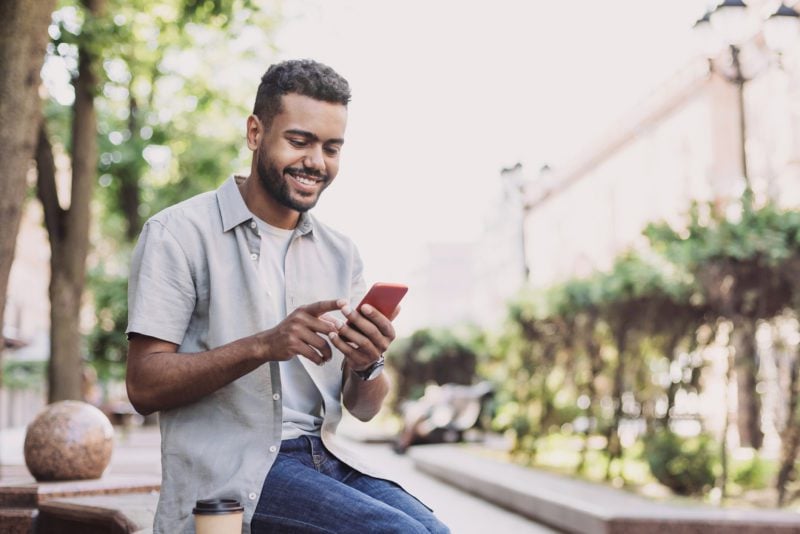 Cheerful young man using smart phone in a city young man reading an expat forum on his cell phone