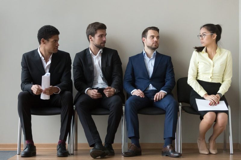 Diverse male employees look at an Asian female employee skeptically