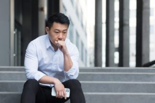 Expat businessman sitting on steps outside office suffering from culture shock