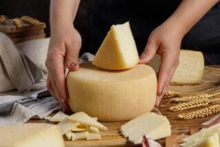 Close-up of hands touching a fresh homemade wheel of cheese on a wooden board