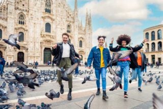 Group of four people friends running in Duomo Square in Milan, celebrating laughing