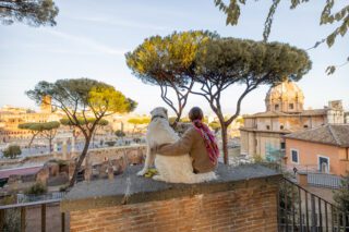 a woman and dog sitting on a wall overlooking the city, enjoying the reality of living in Rome