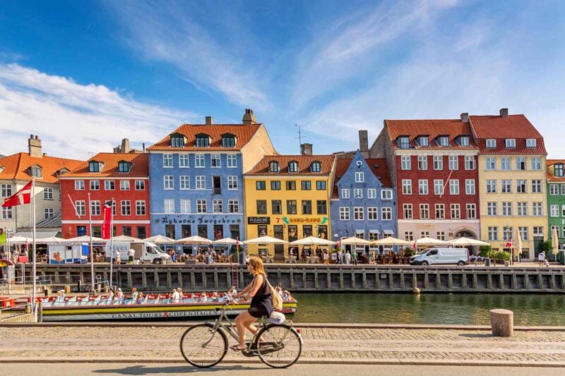 copenhagen-denmark a woman cycling past Nyhavn harbor in Copenhagen, one of the best places to live in Europe
