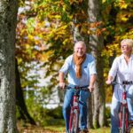 A happy senior couple cycling on bicycles through a leafy park, having made the decision to retire in Germany