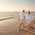 A smiling couple enjoying a sunset beach walk, having successfully achieved their goal to retire abroad