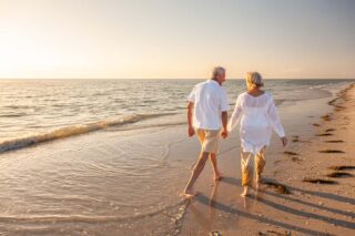 A smiling couple enjoying a sunset beach walk, having successfully achieved their goal to retire abroad