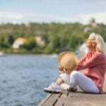 Senior woman sitting peacefully on the edge of a dock, gazing out to sea, feeling grateful for her decision to retire in Sweden.