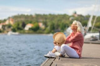 A senior woman sitting peacefully on the edge of a dock, gazing out to sea, feeling grateful for her decision to retire in Sweden.