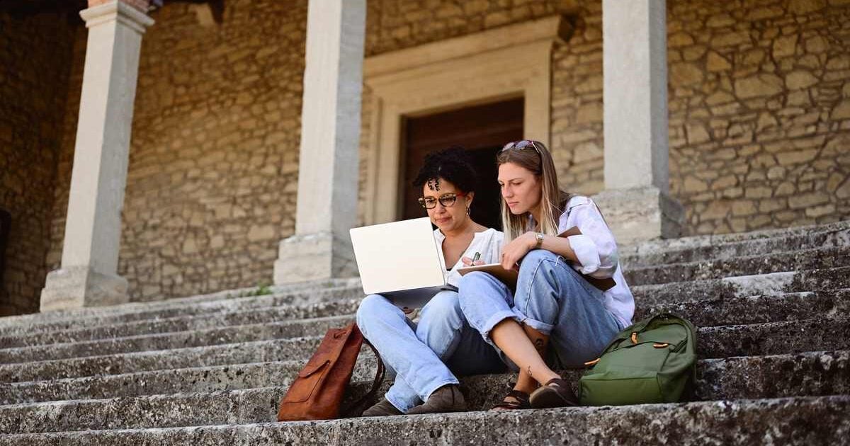 two university students sitting on stairs outside a building on campus in Italy