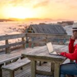 a digital nomad working abroad on his laptop by the beach
