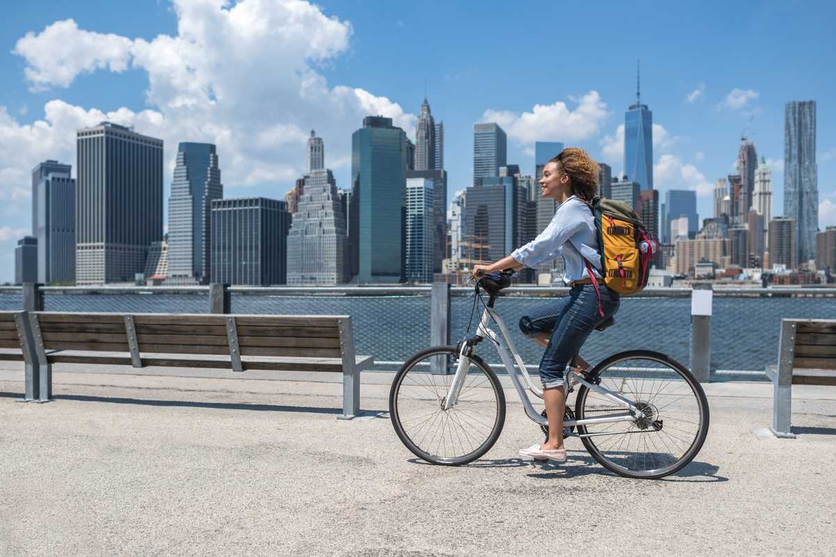 a happy woman cycling alongside the New York skyline, indicating the high average cost of living in the U.S.
