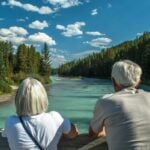 An elderly couple looking out onto a lake in Canada, having made the decision to retire in Canada