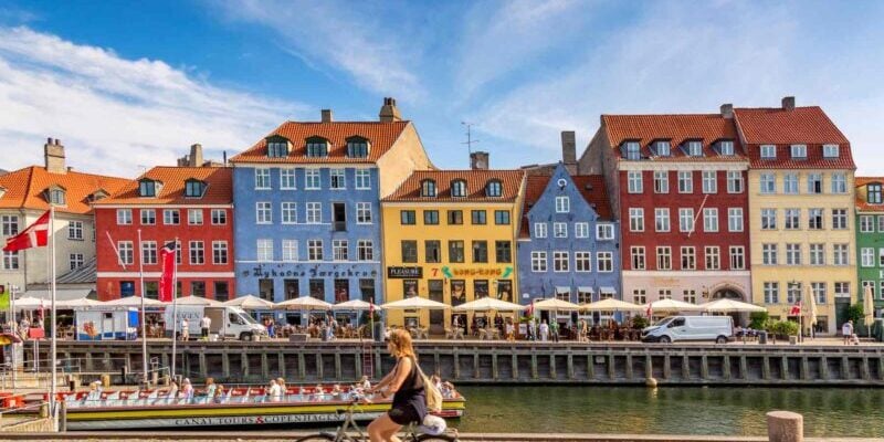 copenhagen-denmark a woman cycling past Nyhavn harbor in Copenhagen, one of the best places to live in Europe