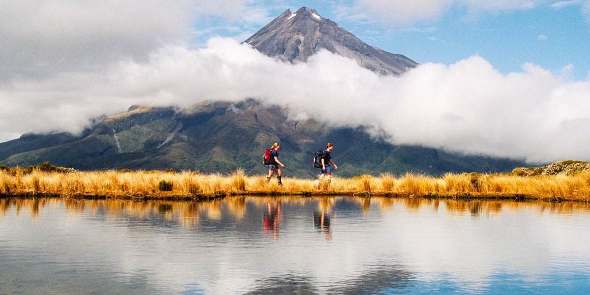 hikers walking along a lake against the backdrop of Mount Taranaki, where the cost of living in New Zealand is more affordable