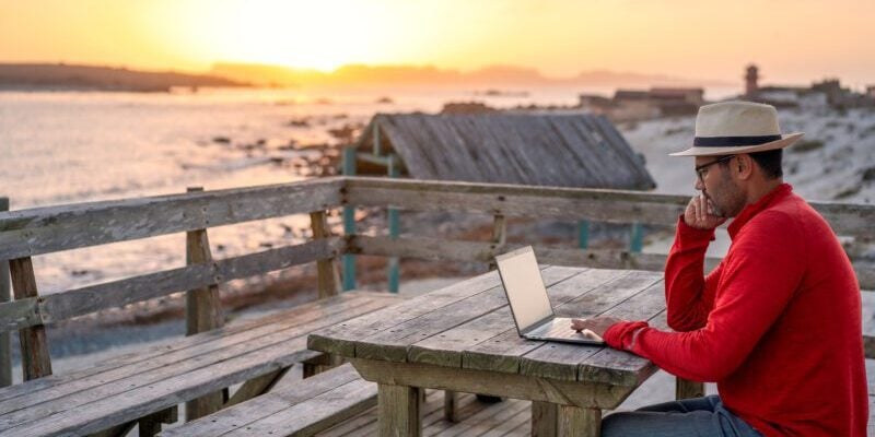 digital nomad sitting outdoors on the beach with a laptop alone doing telecommuting at sunset in brazil digital nomad sitting outdoors on the beach with a laptop alone doing telecommuting at sunset in brazil