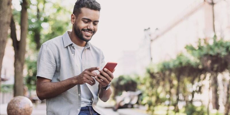Cheerful young man using smart phone in a city young man reading an expat forum on his cell phone